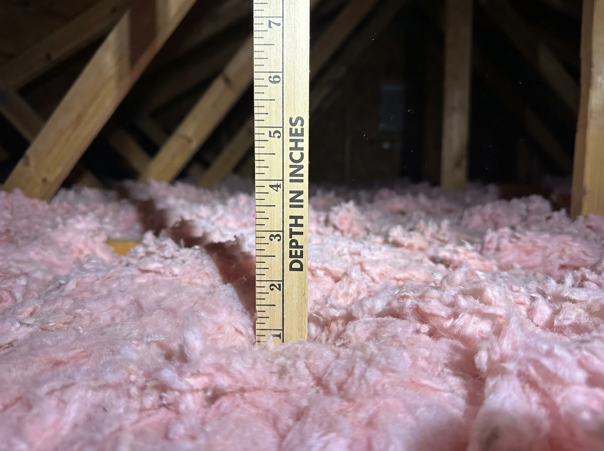Inspection documentation photo: a depth ruler standing in deep blown-in attic insulation