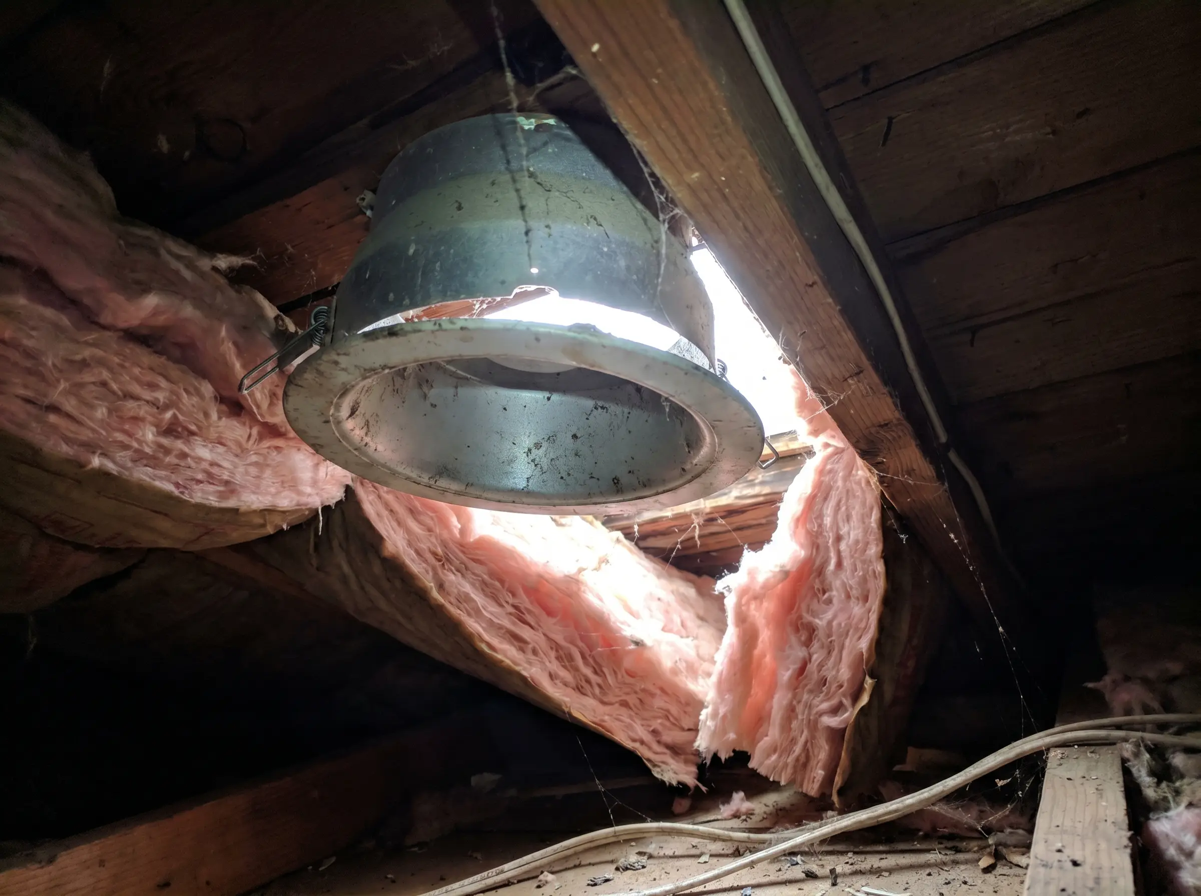 Raw photo: light leaking up around an old pot light housing seen from the attic